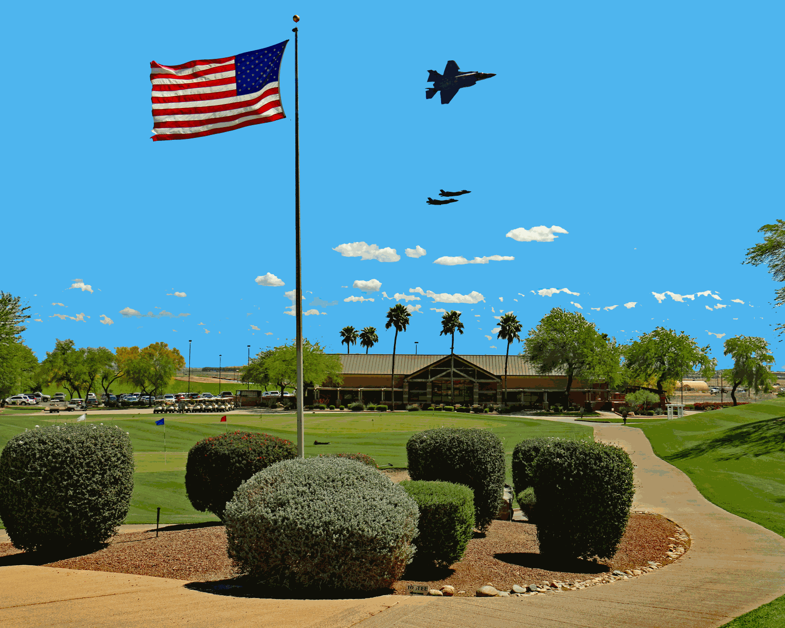 Picture of Falcon Dunes golf course with a United States Flag in the foreground and the clubhouse in the background with two planes overhead.